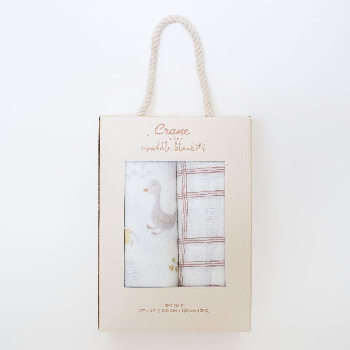 A boxed set of two swaddle blankets hanging from a cream rope handle. The package is cream-colored cardboard with a clear window showing one white swaddle with a gray duck illustration and one white plaid swaddle with muted red stripes.