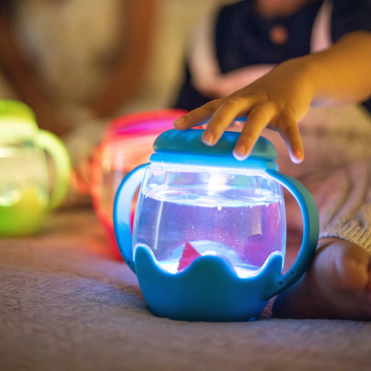 Child's hand holding a glowing blue sippy cup on a soft surface