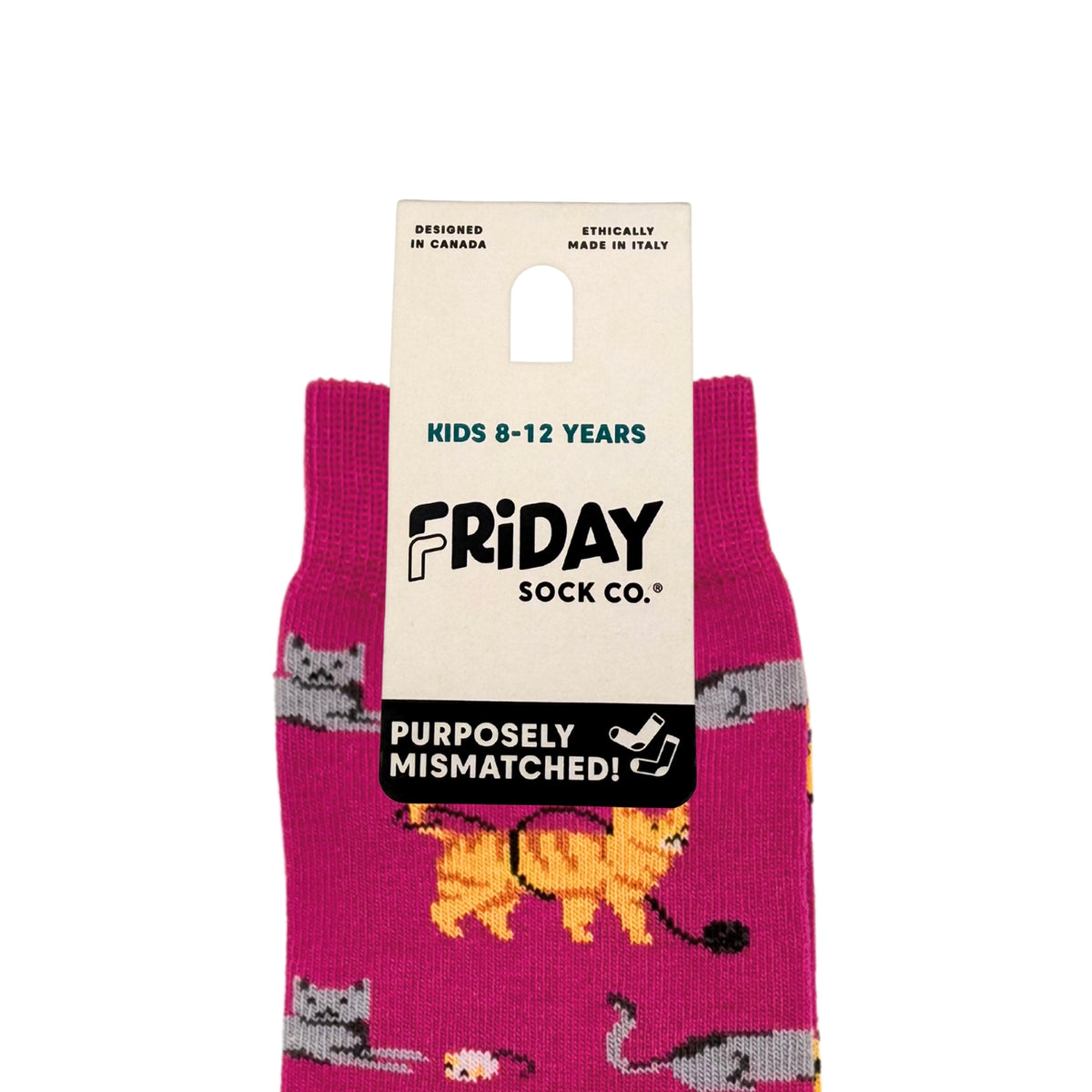 A pair of kids' mismatched socks by Friday Sock Co. in a bright magenta pink color, featuring a pattern of gray cats and a yellow/orange cat, attached to a cream-colored cardboard hanger with product details.