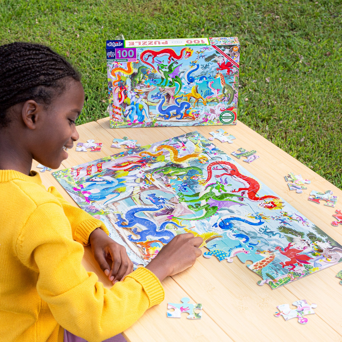 Child working on a dinosaur-themed puzzle outdoors with a colorful puzzle box in the background.