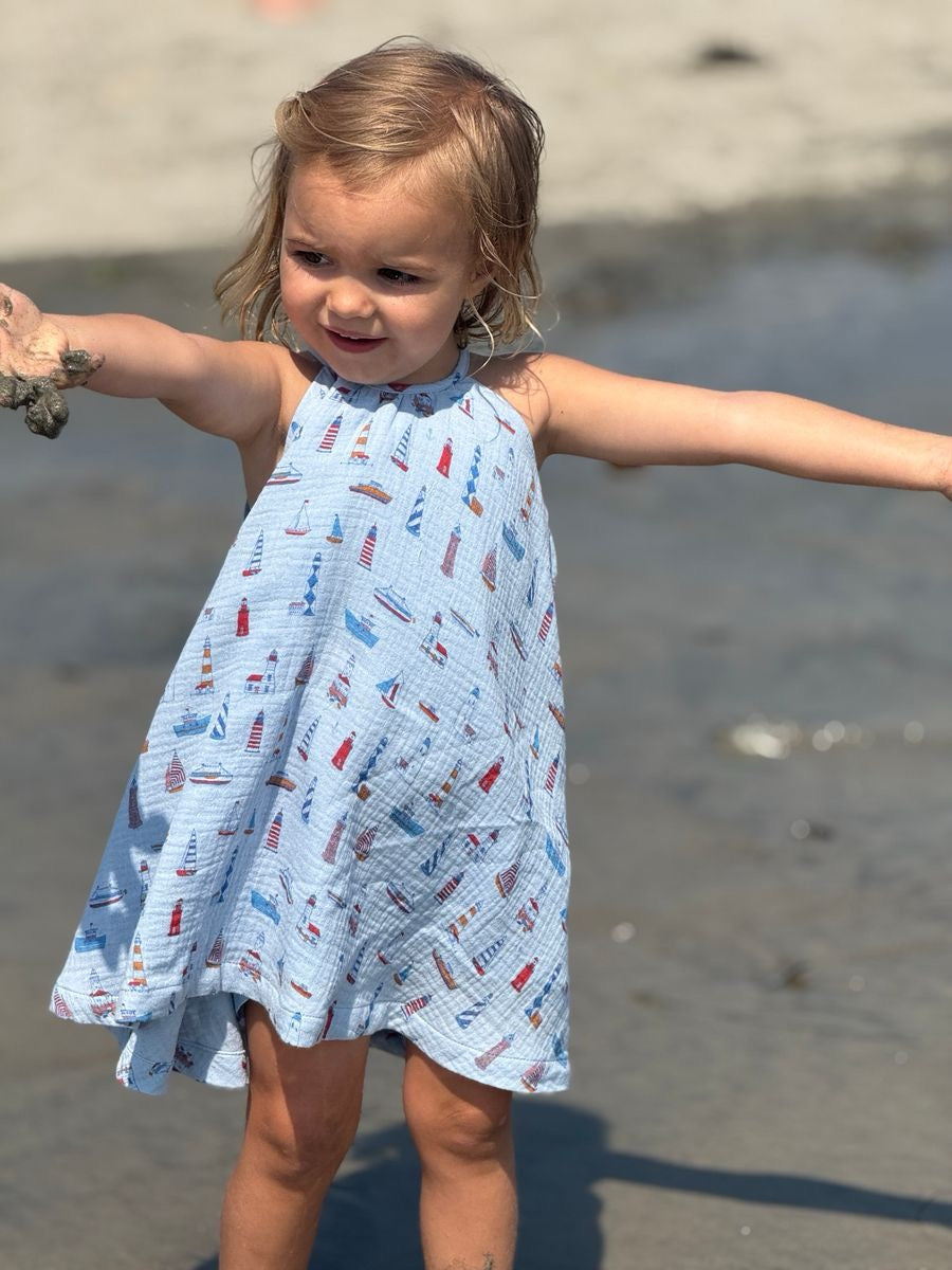 Child in a blue dress with boat pattern standing on a beach