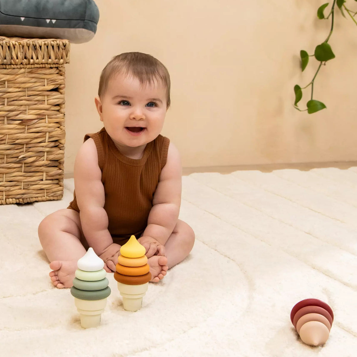 Baby sitting on a white blanket with colorful wooden toys, smiling.