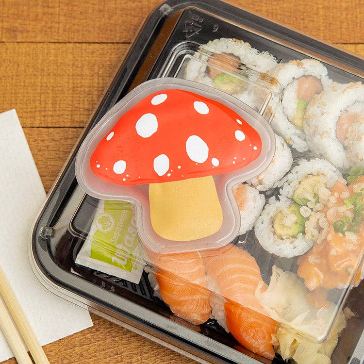 Sushi and sashimi in a bento box with a red mushroom-shaped lid on a wooden surface.