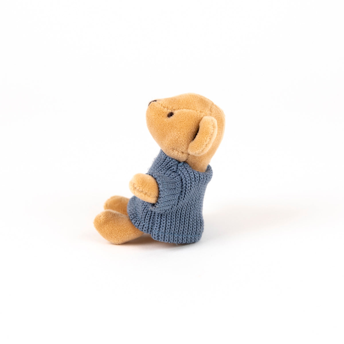 A small plush teddy bear sitting upright, wearing a knitted blue sweater, photographed on a clean white background.