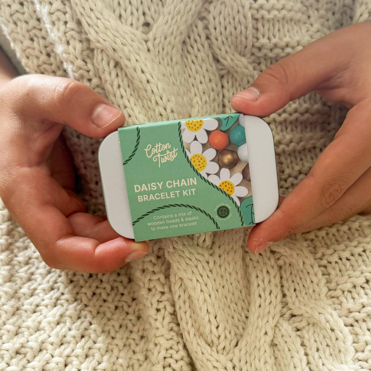 Person holding a 'Daisy Chain Bracelet Kit' against a knitted fabric background
