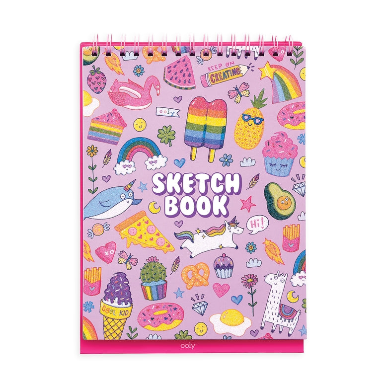 A pink spiral-bound sketchbook with a colorful cartoon illustration pattern, featuring the words 'SKETCH BOOK' on the cover, photographed against a plain white background.