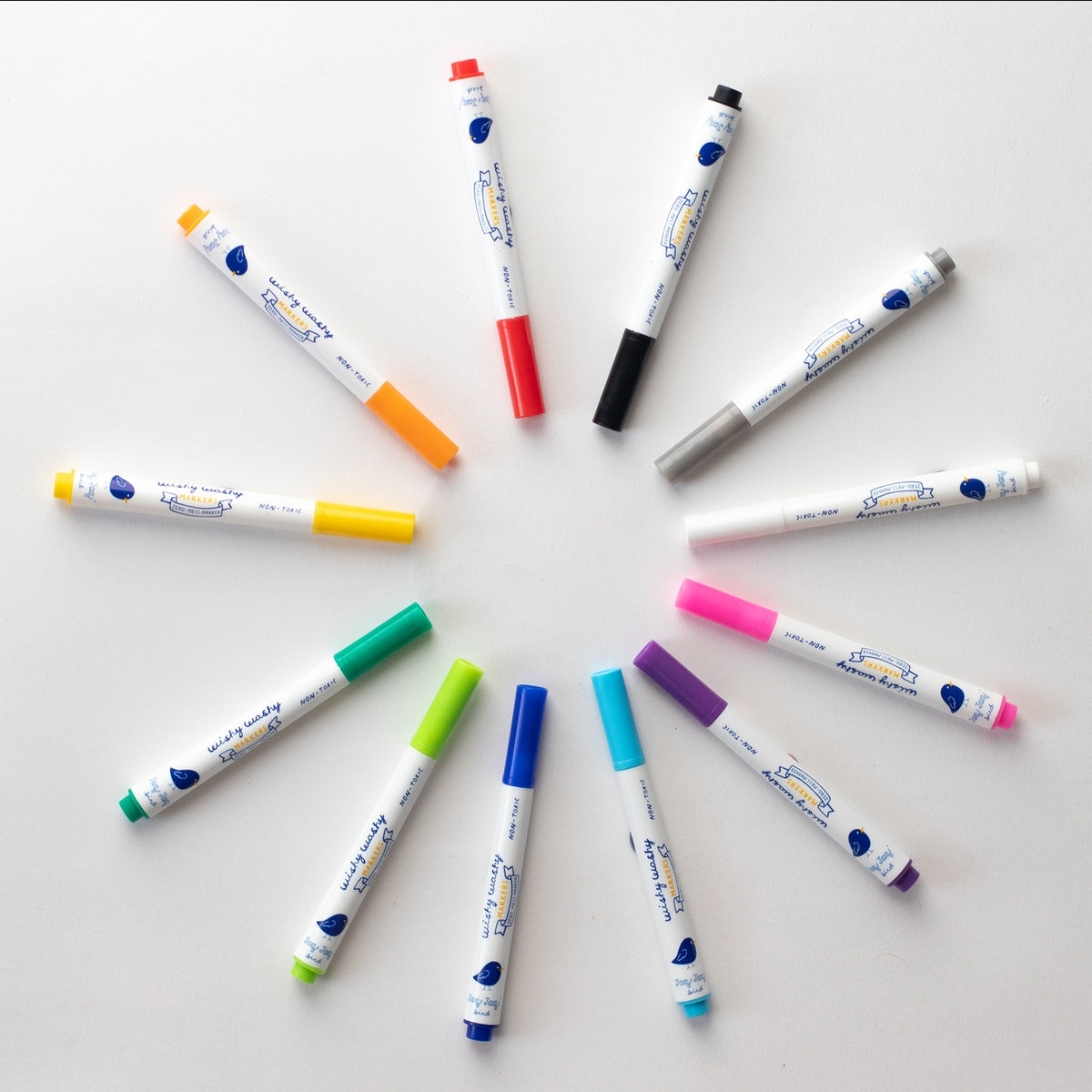Twelve white dual-tip marker pens with blue printed labels and various colored caps are arranged in a circular pattern on a light gray background.