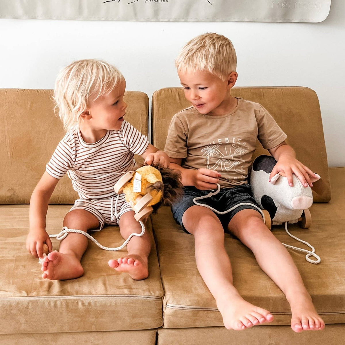 Two young children sitting on a couch with toys, one holding a toy lion and the other a toy cow.
