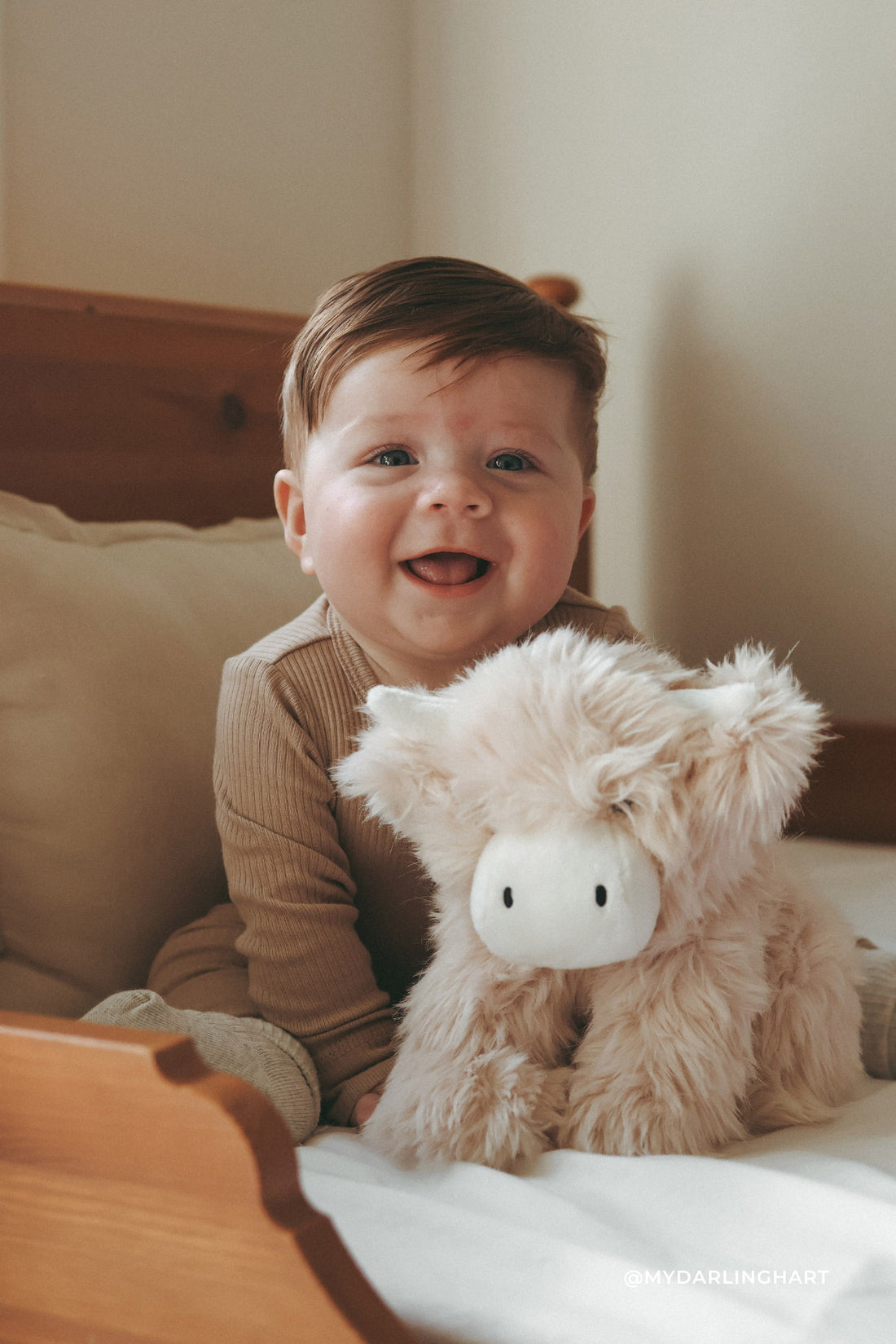 Child holding a plush toy on a bed with a neutral background