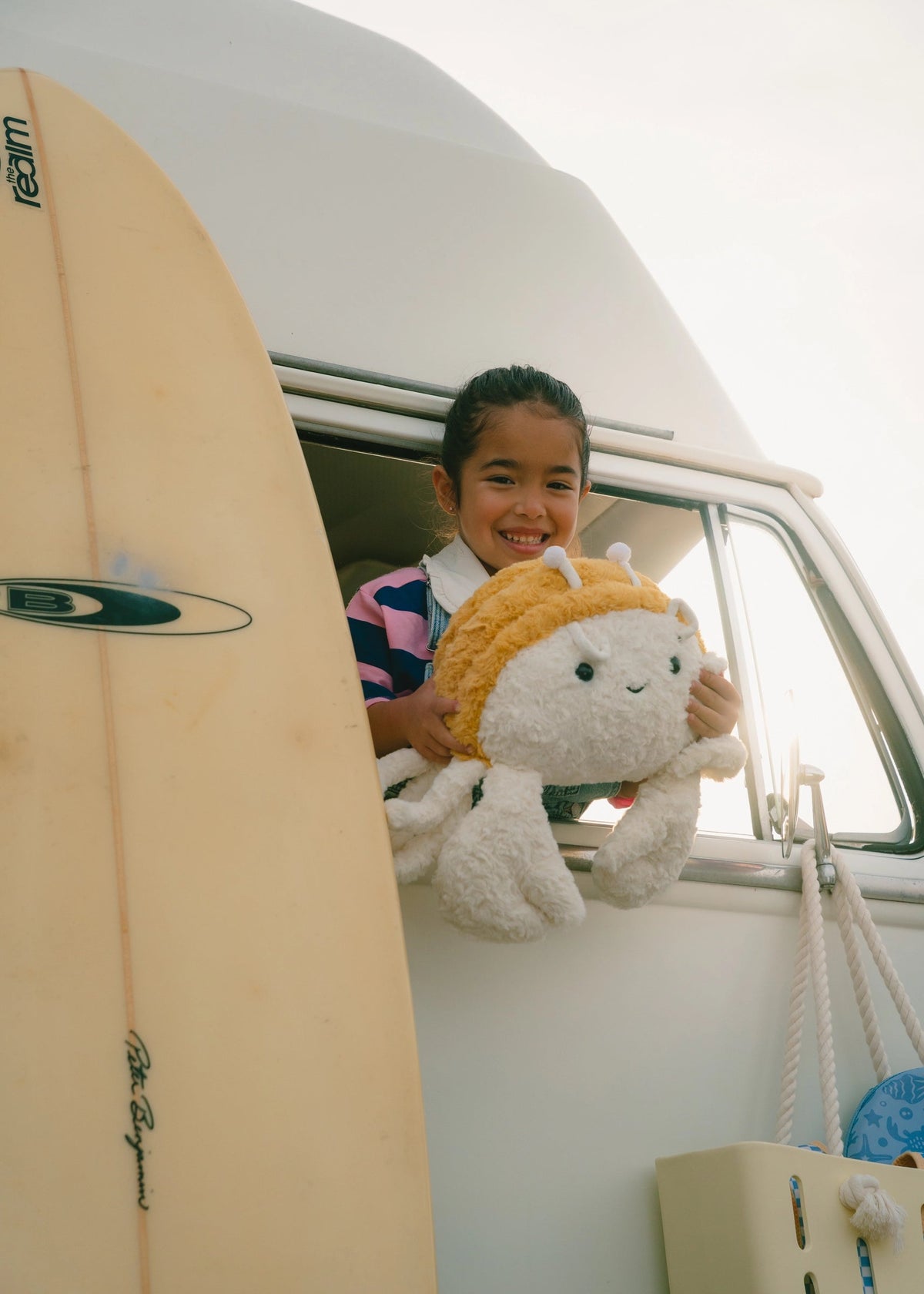 Child holding a plush toy with a surfboard next to a van
