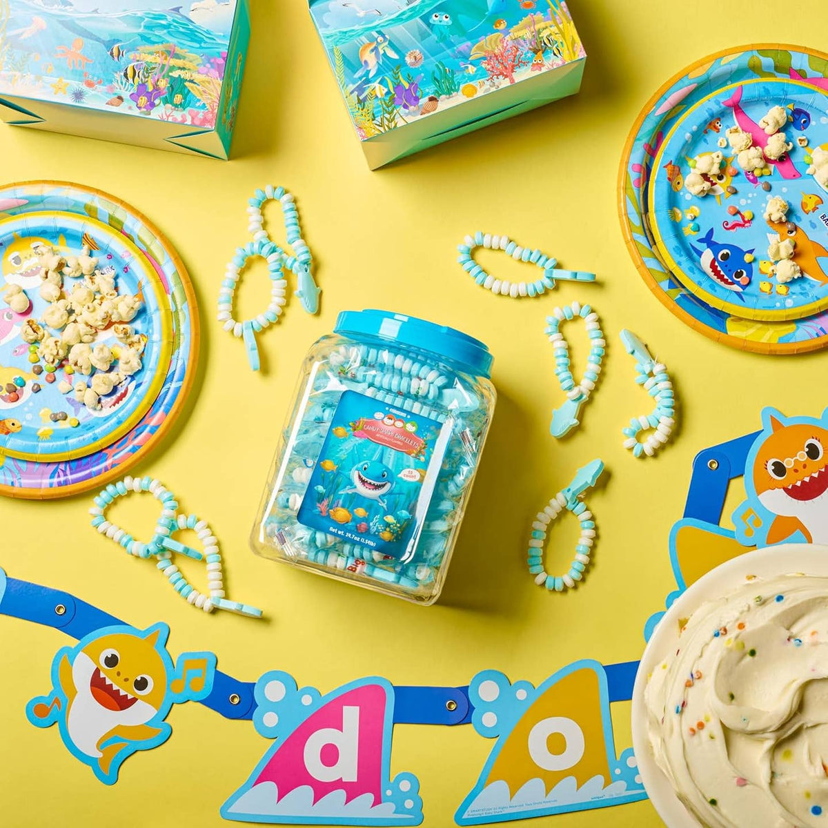 Baby Shark-themed party supplies including plates, cups, and candy on a yellow background