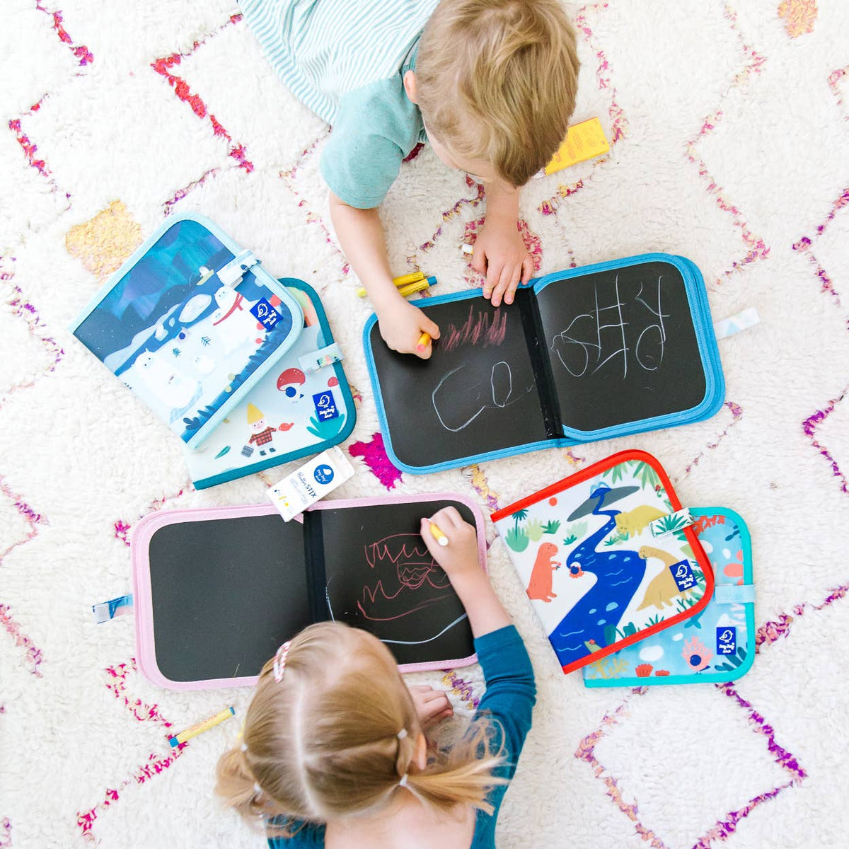 Two children playing with colorful drawing boards on a patterned rug.