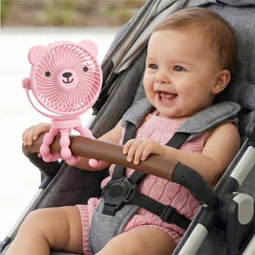 Baby in a stroller holding a pink bear-shaped fan