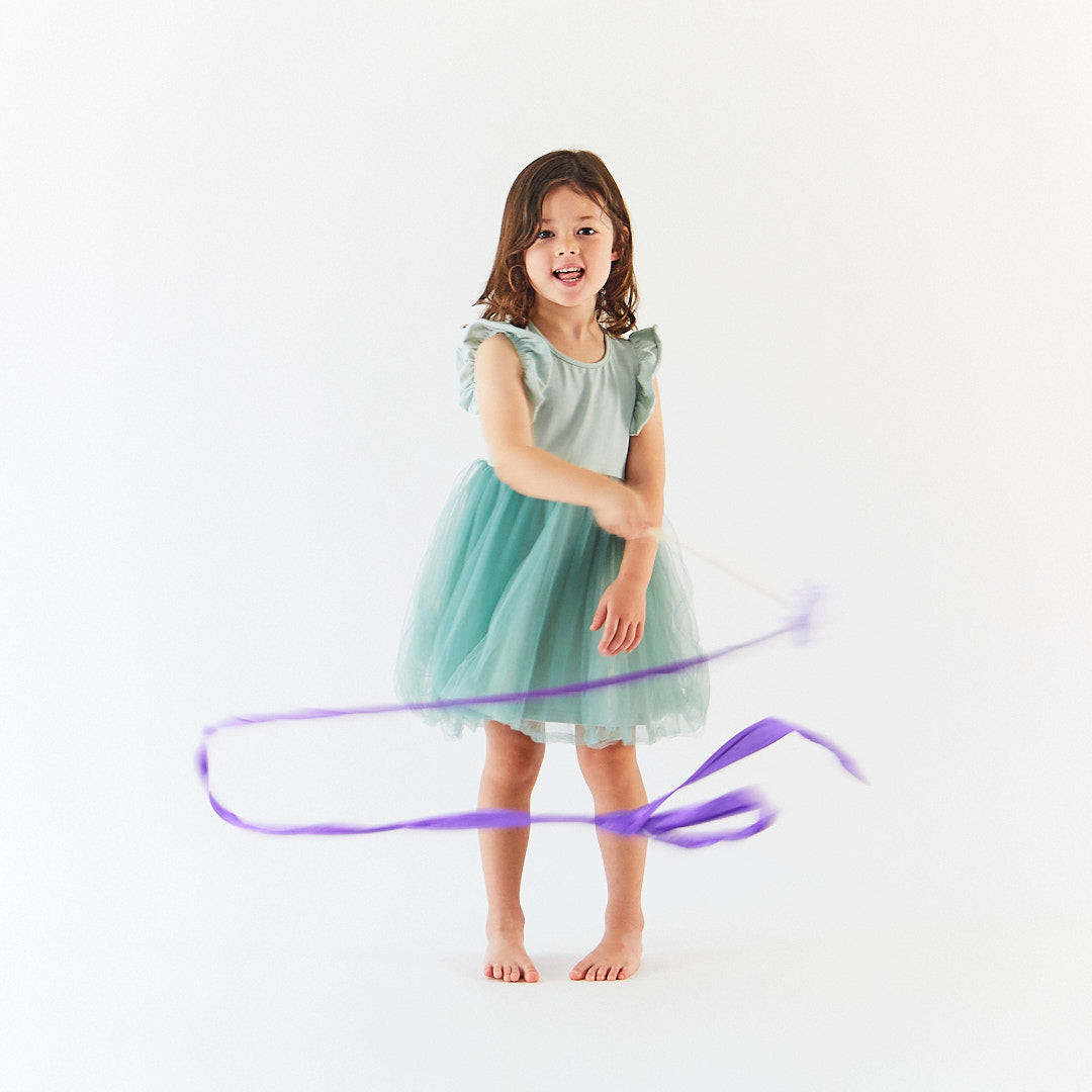 Young girl in a light blue dress holding a purple ribbon against a white background