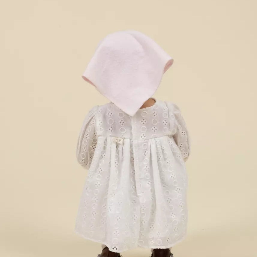 Child wearing a white dress with lace details and a pink hood on a beige background