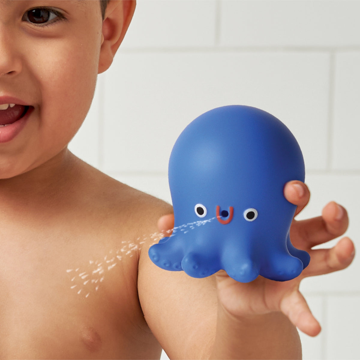 Child holding a blue octopus-shaped toy with water features, against a bathroom background.