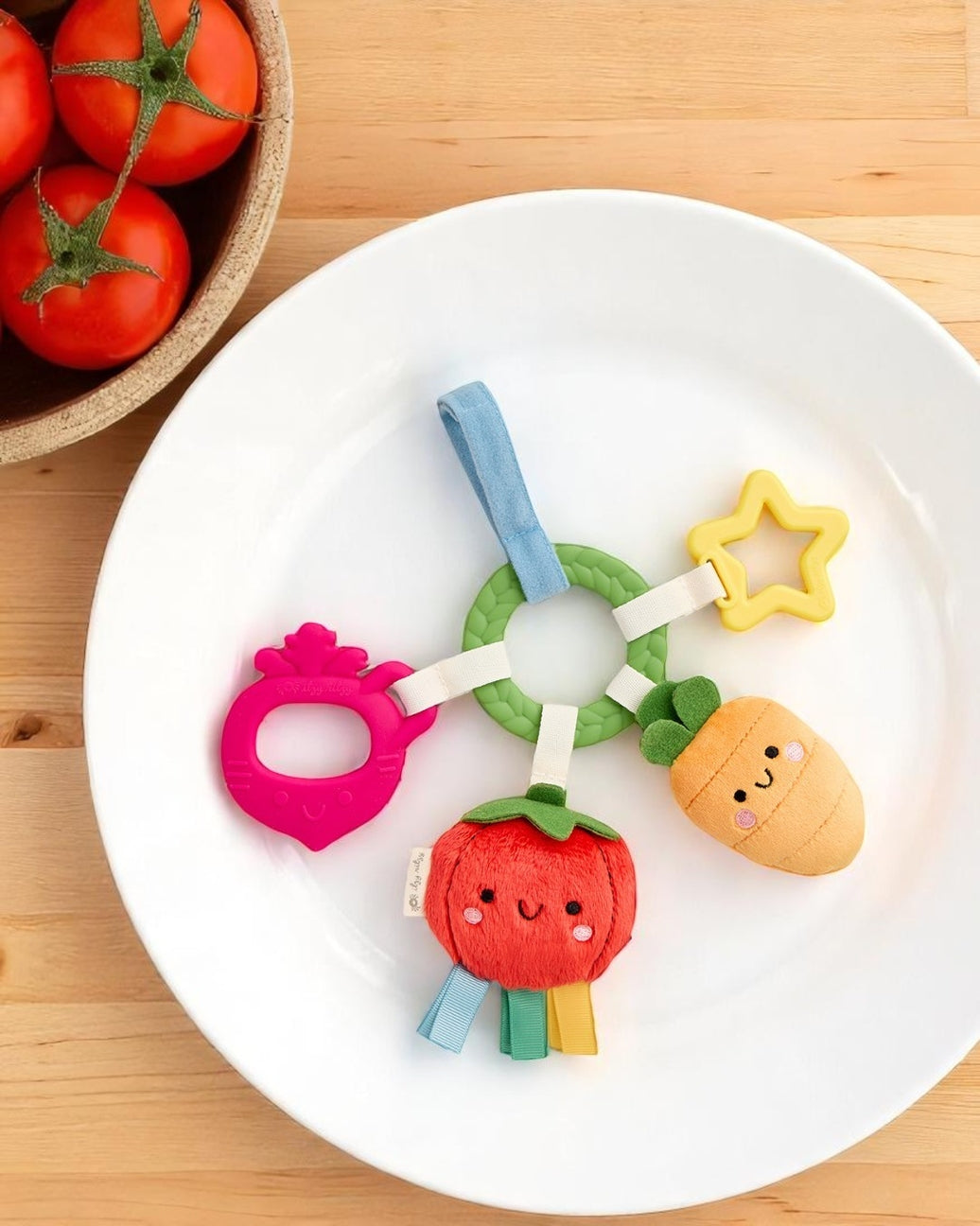 Colorful baby teething toy on a white plate with tomatoes in the background
