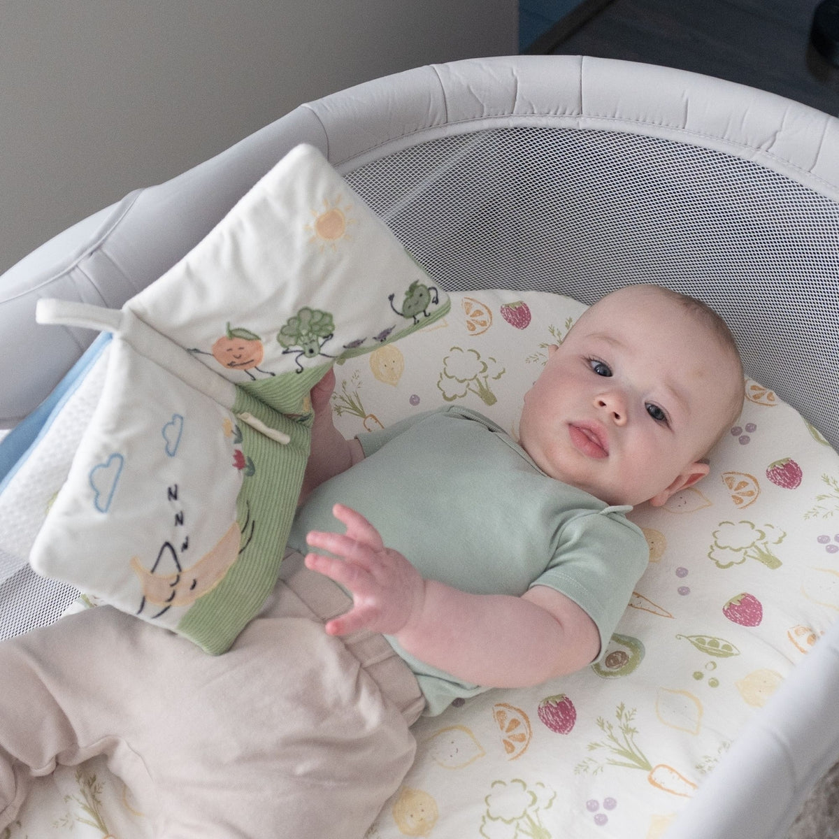 Baby lying in a crib with a soft toy, surrounded by colorful bedding
