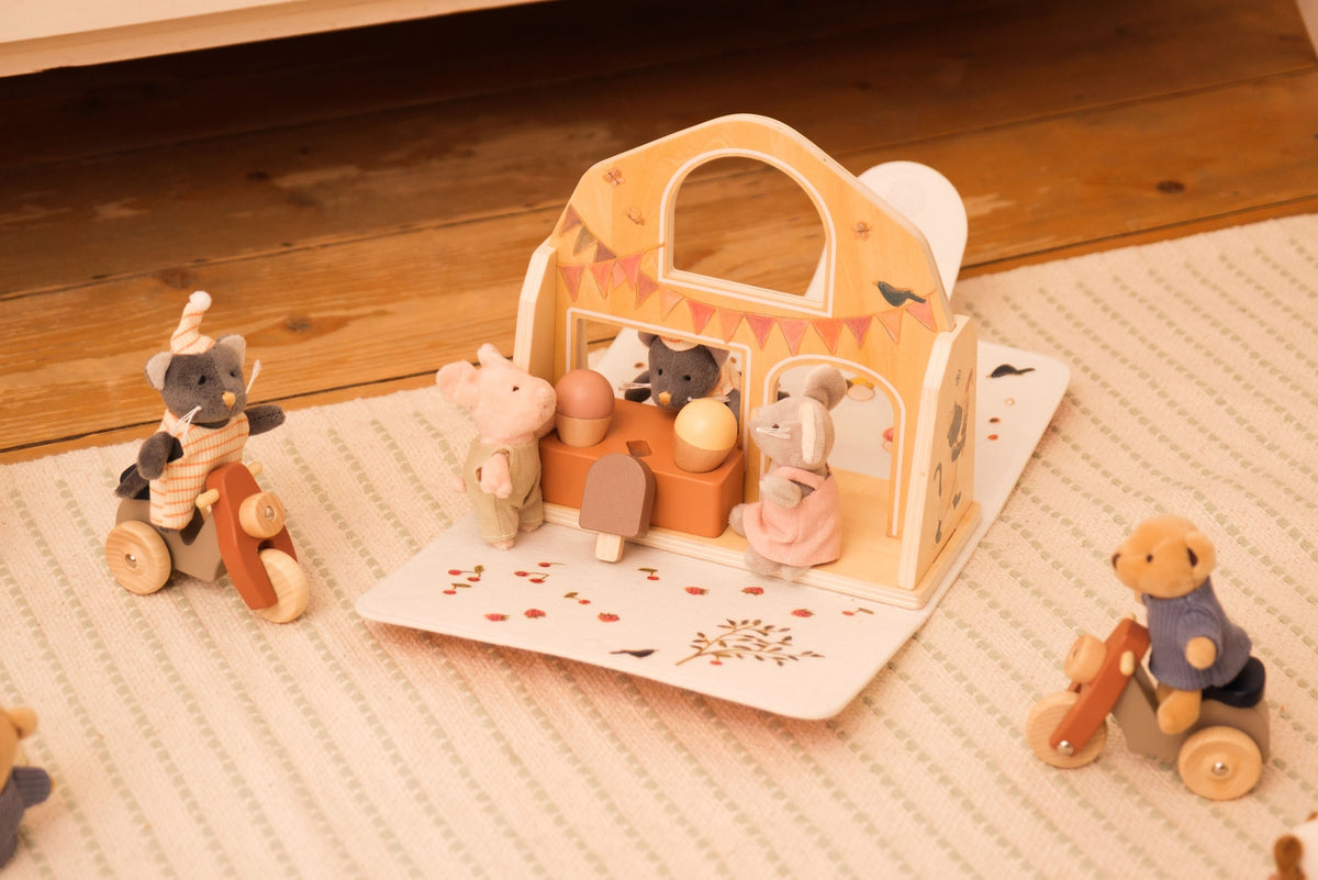 Wooden toy set with animals around a small house on a textured surface.