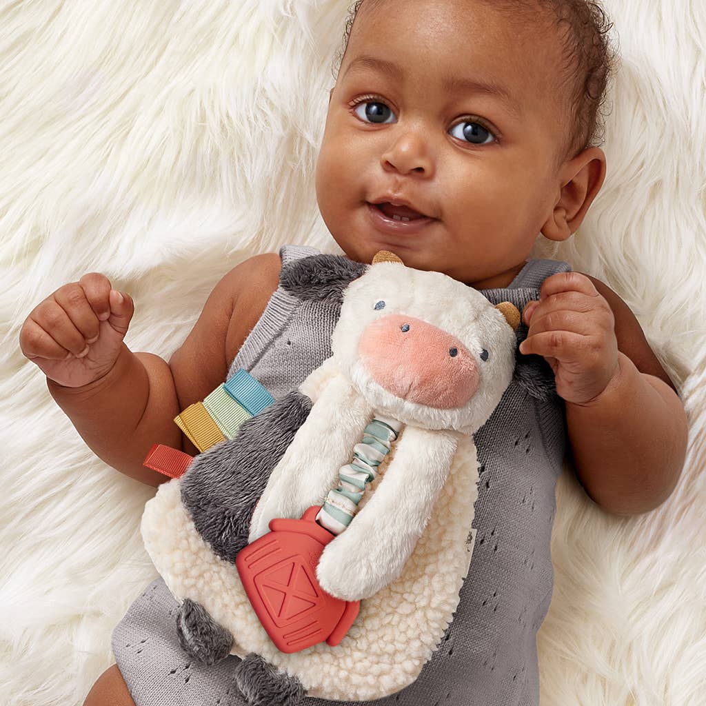 Baby holding a soft toy with colorful accents on a white fluffy blanket