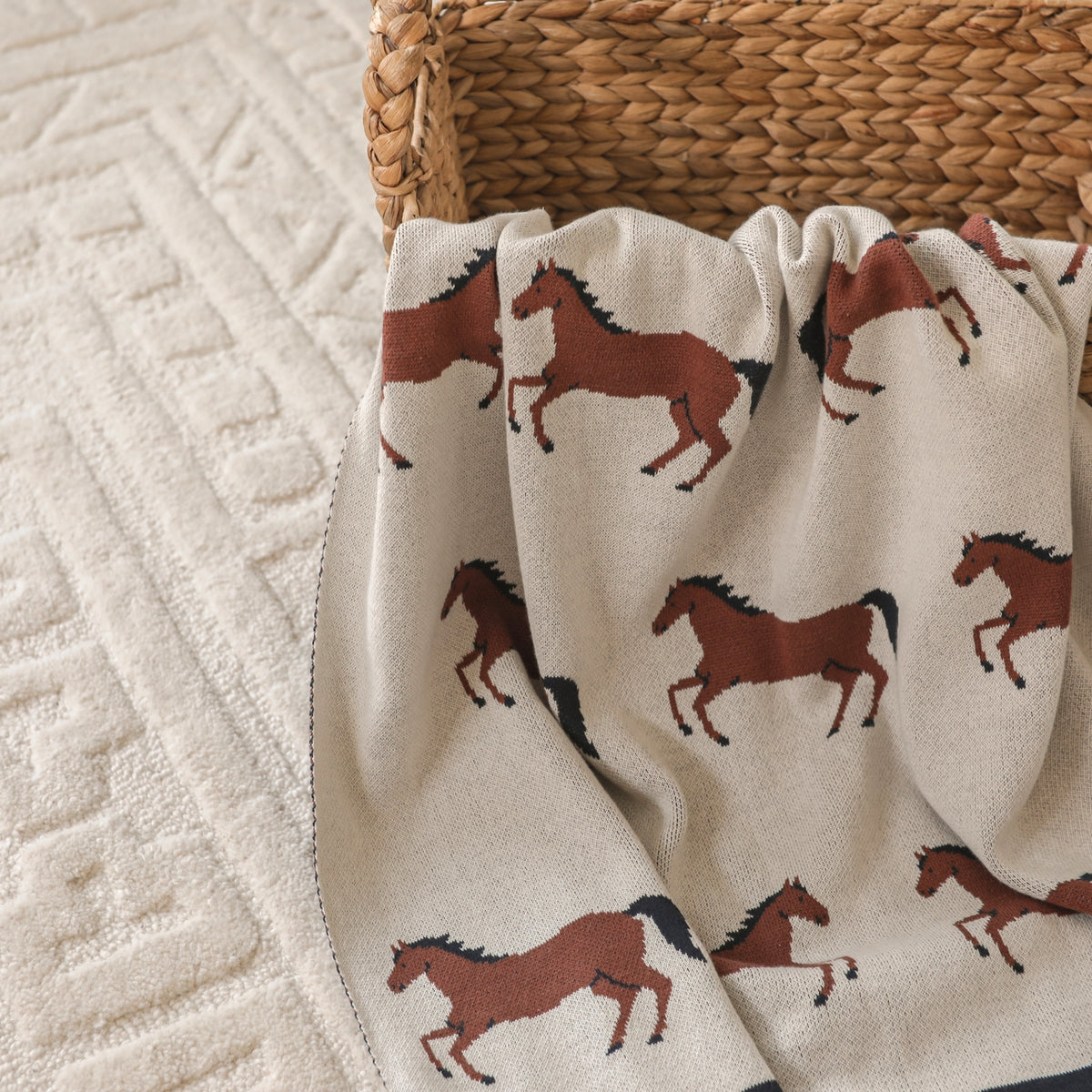 Blanket with horse pattern draped over a woven basket on a textured surface