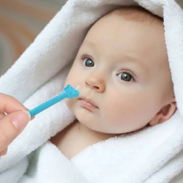 Baby being shown a blue toothbrush with a white towel draped over them