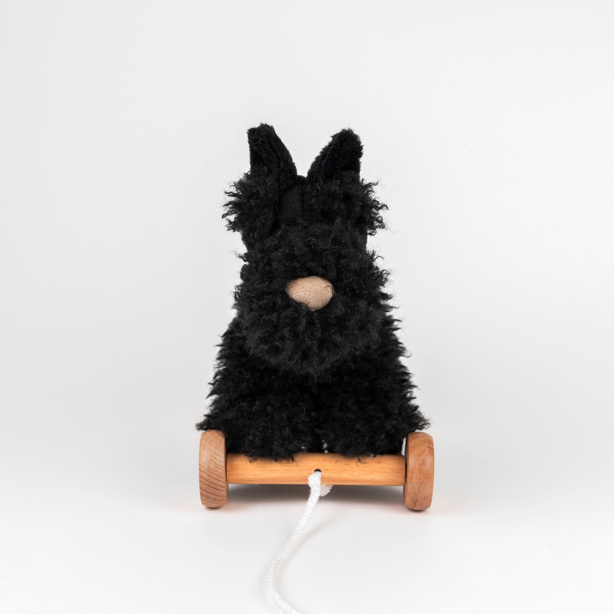 Black plush toy on wooden wheels with a white background