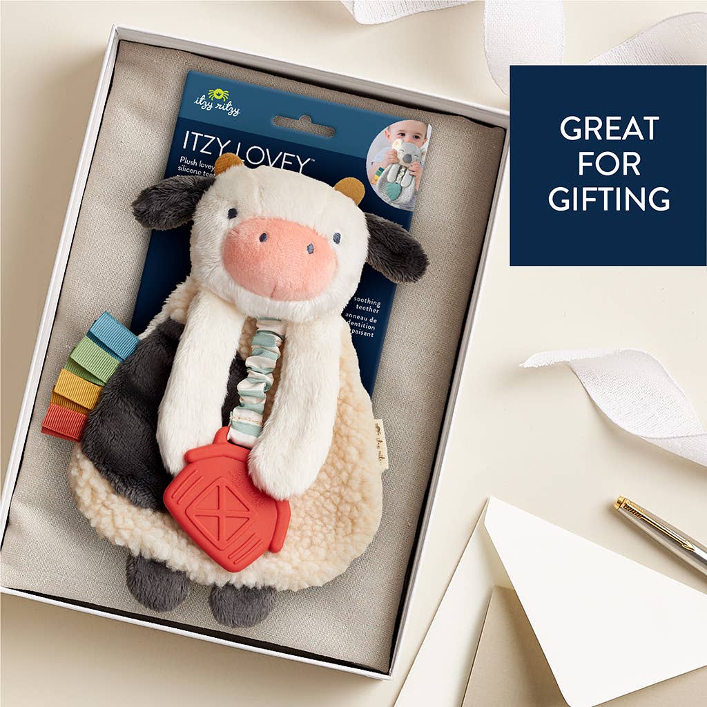 Cow-shaped toy with a red teether in a box, labeled 'Itzy Lovey', on a light background.