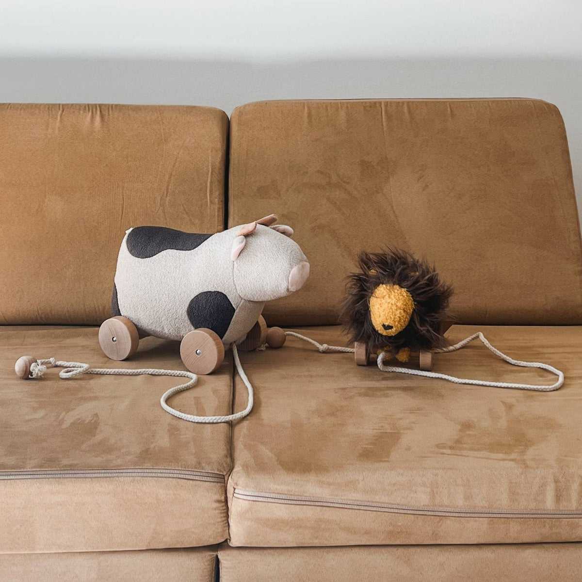 Two pull toys, a cow and a lion, on a brown sofa.