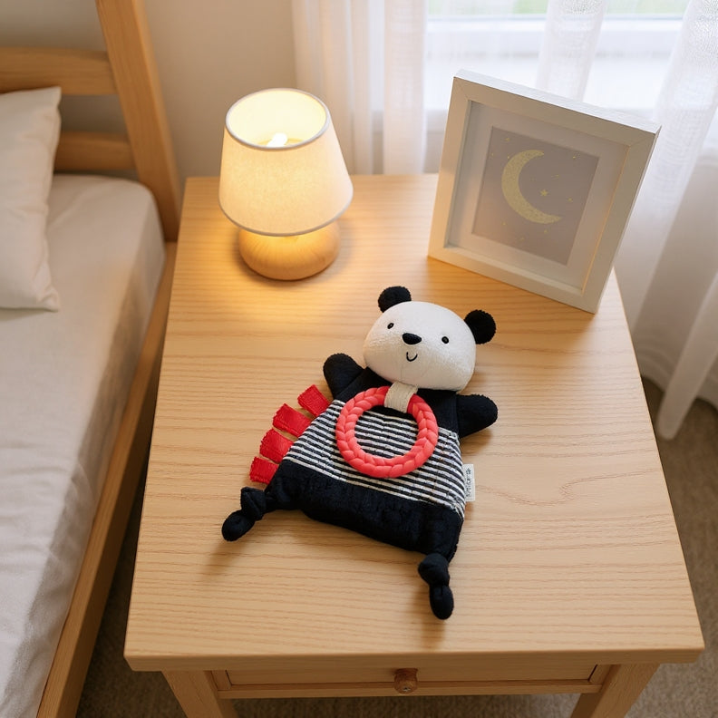 Panda-shaped toy with a red ring on a wooden nightstand next to a bed and lamp.