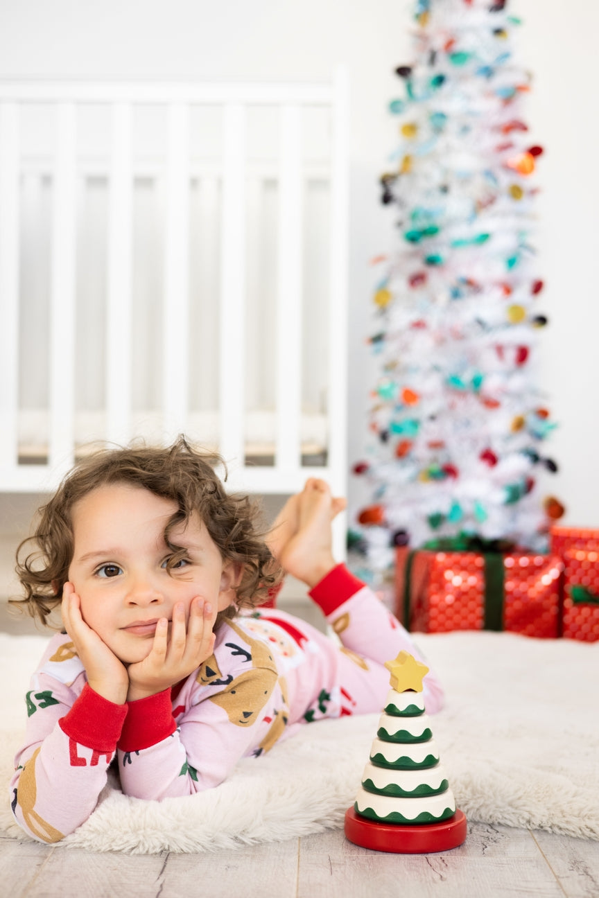Child in pajamas with a Christmas tree toy and decorated tree in the background