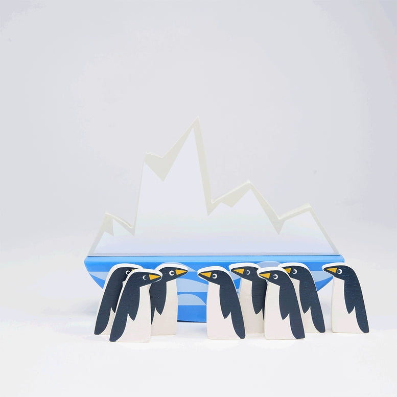 A collection of eight stylized wooden penguins lined up in a row in front of a rocking white iceberg base resting on a blue-and-white wavy ocean design against a clean white background.