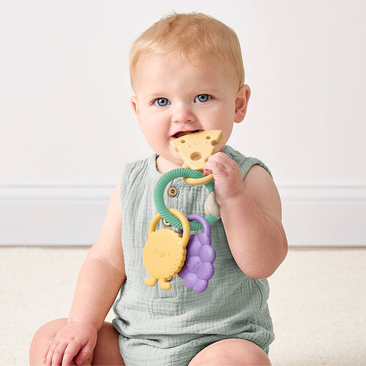 Baby holding a colorful teething toy with a plain background