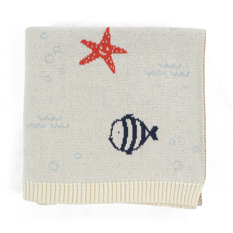 A square knit baby blanket in cream with a red starfish, a navy blue striped fish, and light blue bubble motifs, finished with a ribbed cream border.