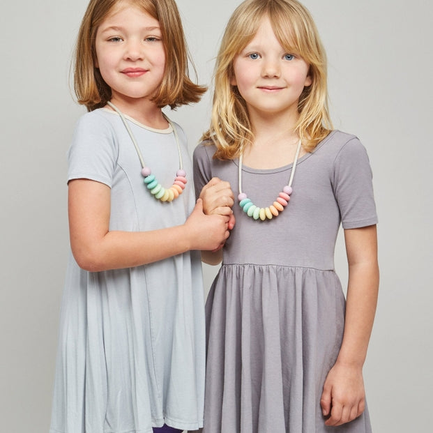 Two young girls wearing gray dresses standing against a plain background