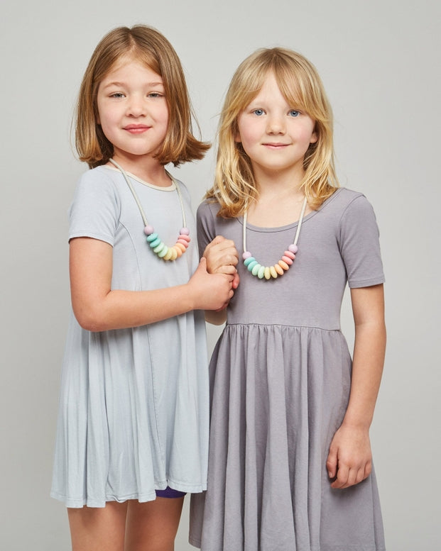 Two young girls wearing gray dresses standing against a plain background