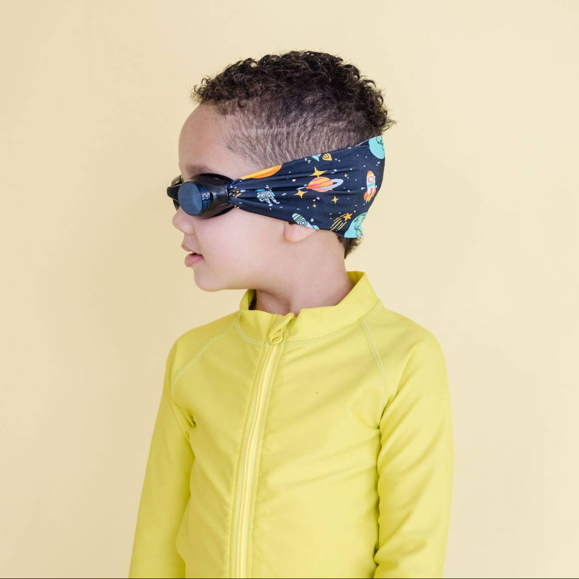 Child wearing a yellow jacket and space-themed headband on a beige background