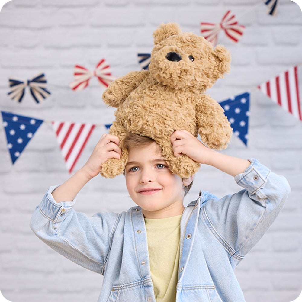 Child wearing a teddy bear on their head with a decorative flag background