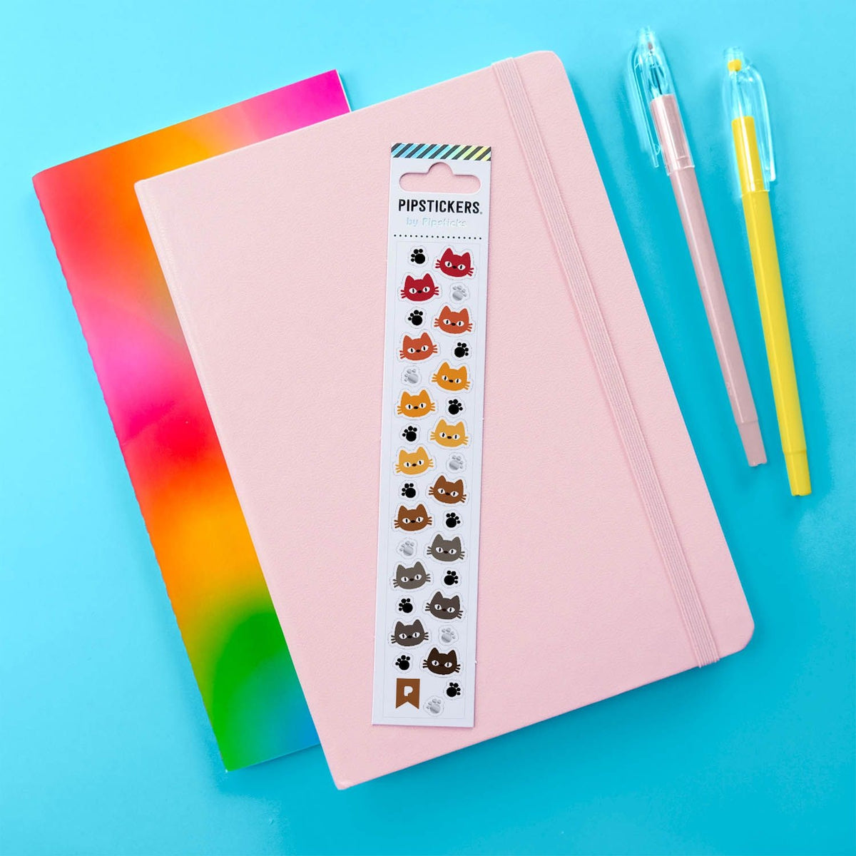 Notebook with cat-themed stickers on a blue background with colorful pens.