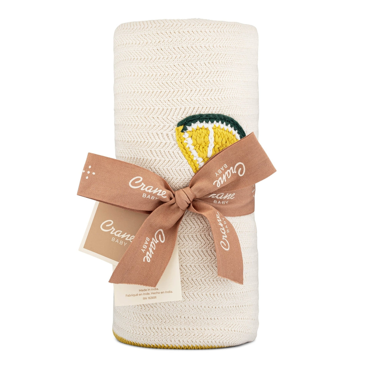 White textured blanket with a embroidered lemon design and a brown ribbon, on a white background.