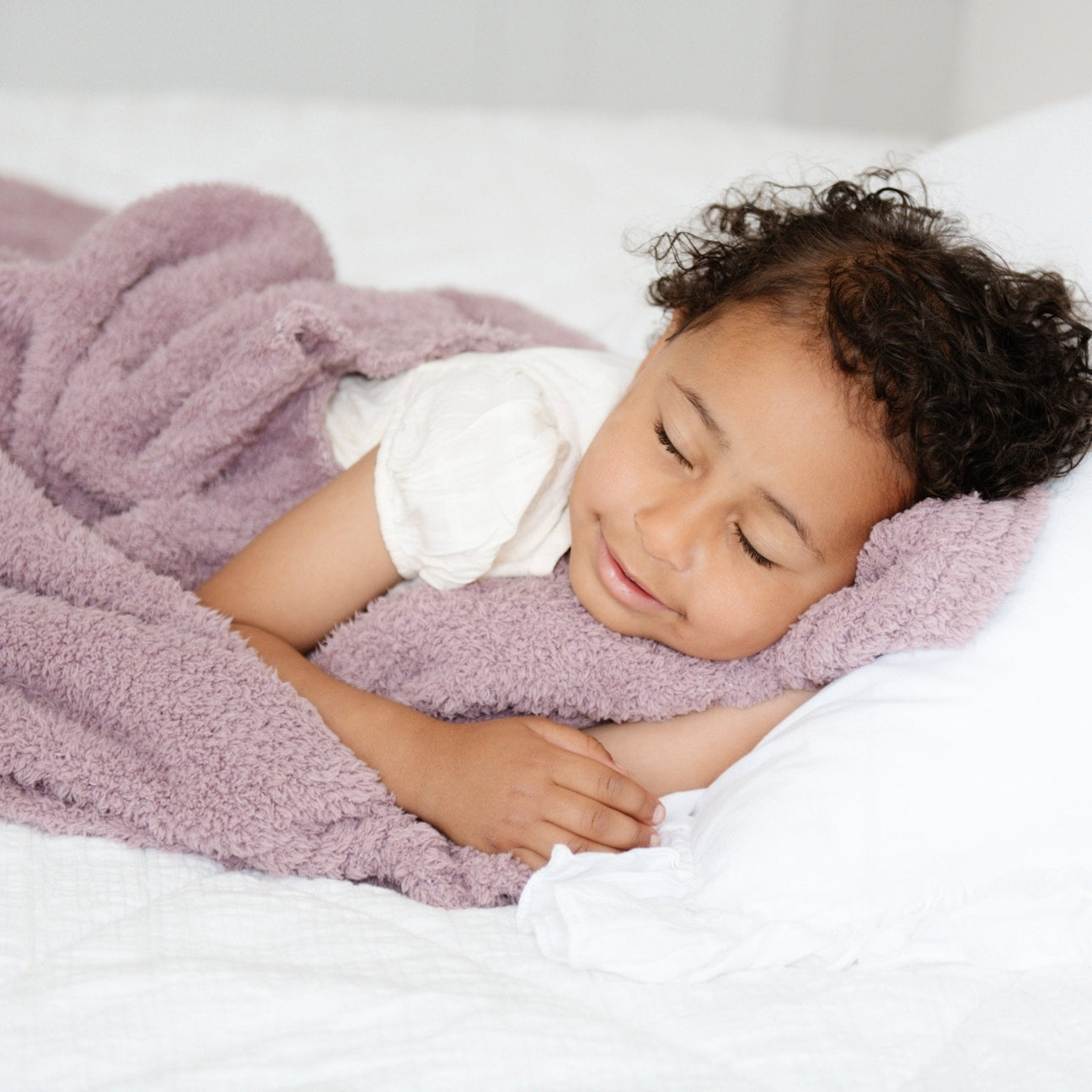 Child lying in bed with pink blanket and white pillow