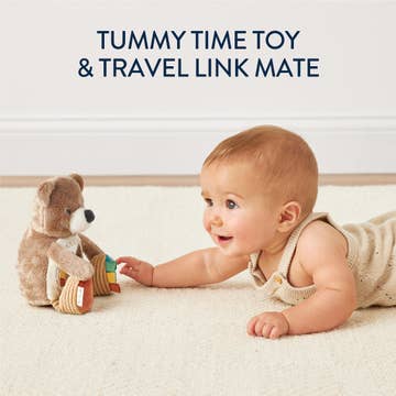 Baby playing with a tummy time toy and travel link mate on a soft surface.