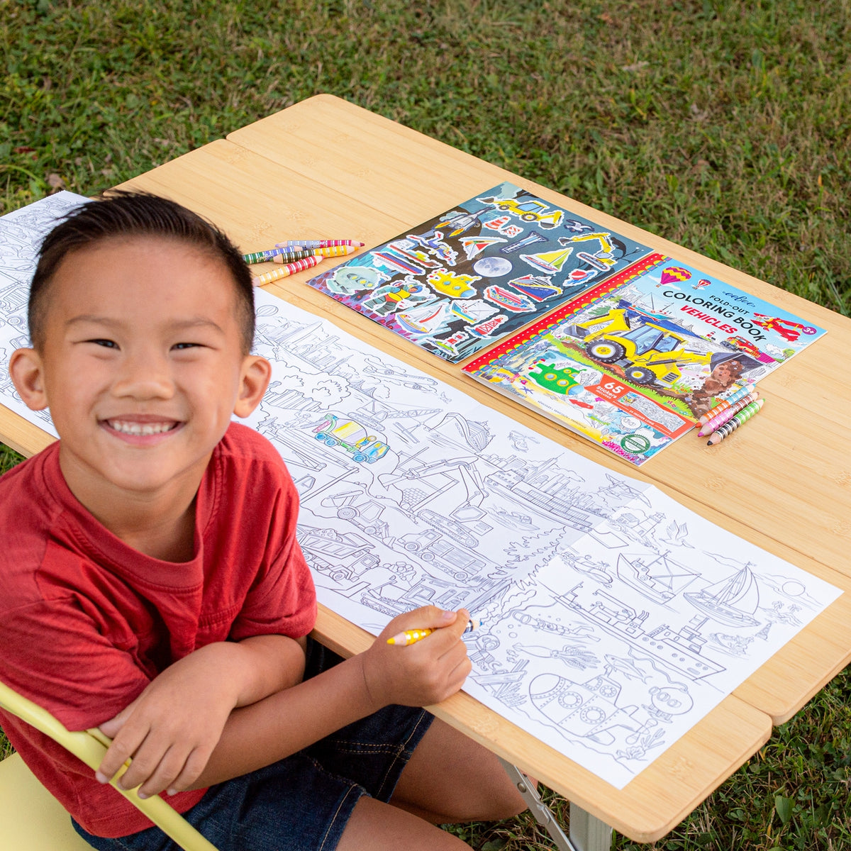 Child coloring at a table with coloring books and crayons outdoors