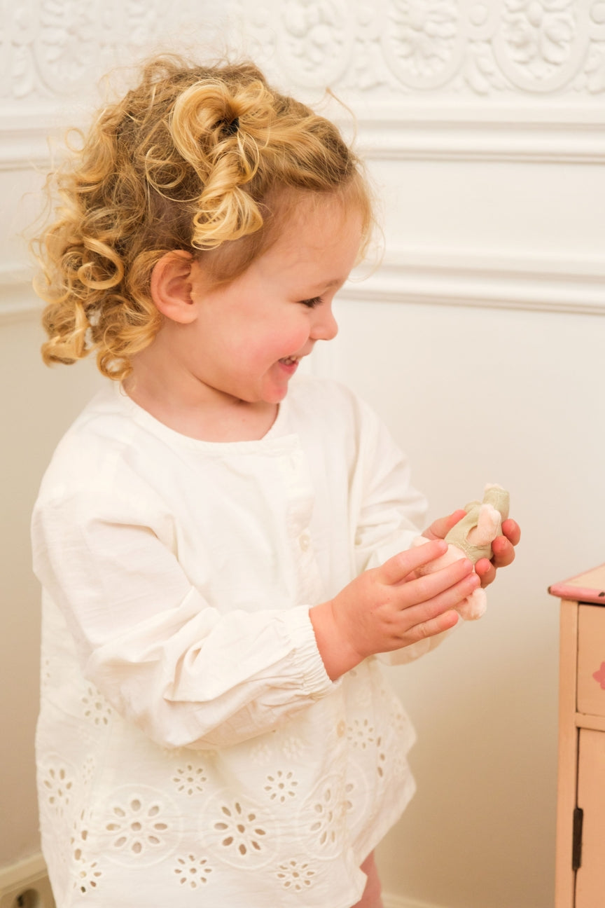 Child in a white dress holding a small object against a neutral background
