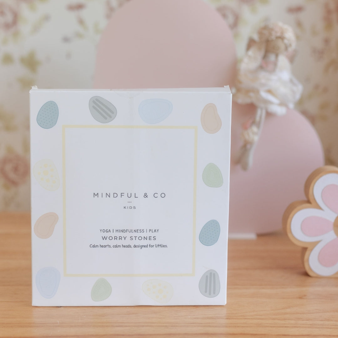 Box of Mindful & Co worry stones on a wooden surface with decorative elements in the background