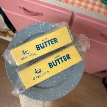 Two packages of butter on a blue plate with a pink background