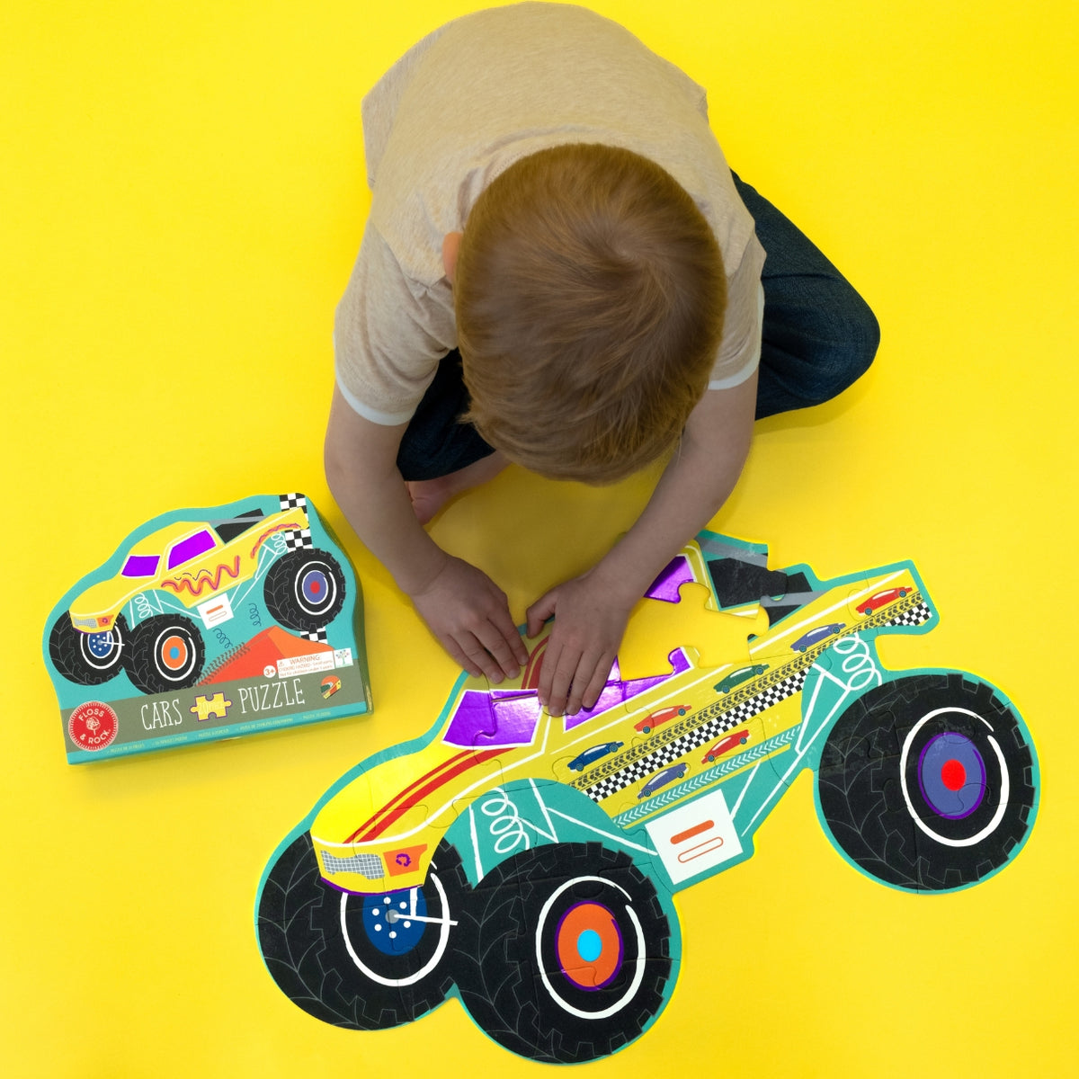 Child playing with a colorful car puzzle on a yellow floor