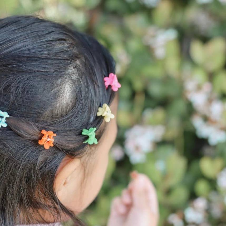 Close-up of a child's hair with colorful hair clips against a blurred natural background