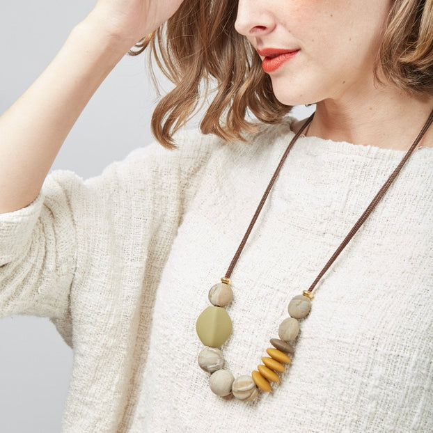 Woman wearing a necklace with large beads on a plain background