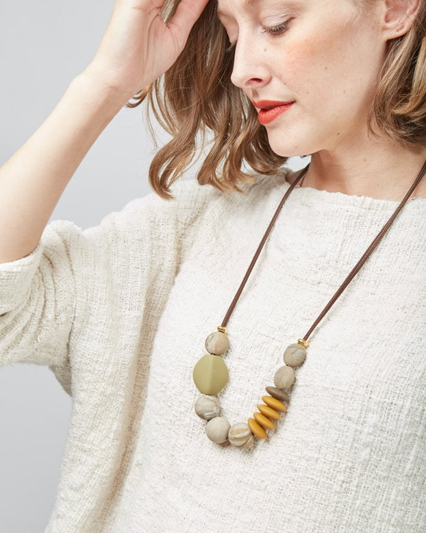 Woman wearing a necklace with large beads on a plain background
